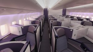 Business class cabin with private lie-flat seats in purple, arranged in individual pods along two aisles.
