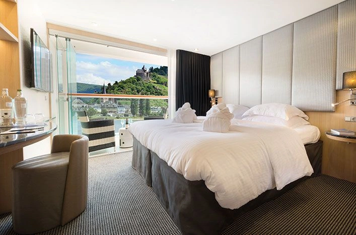 Hotel room with two large beds, white linens, and a balcony overlooking a hillside with a castle in the distance.