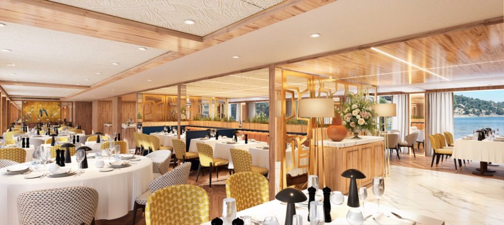 Elegant seaside restaurant dining room with white-tablecloth tables, yellow patterned chairs, and large windows overlooking the water
