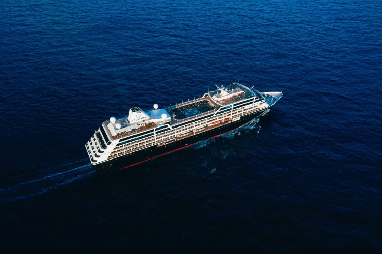 A large cruise ship sailing through calm deep-blue sea from an aerial view