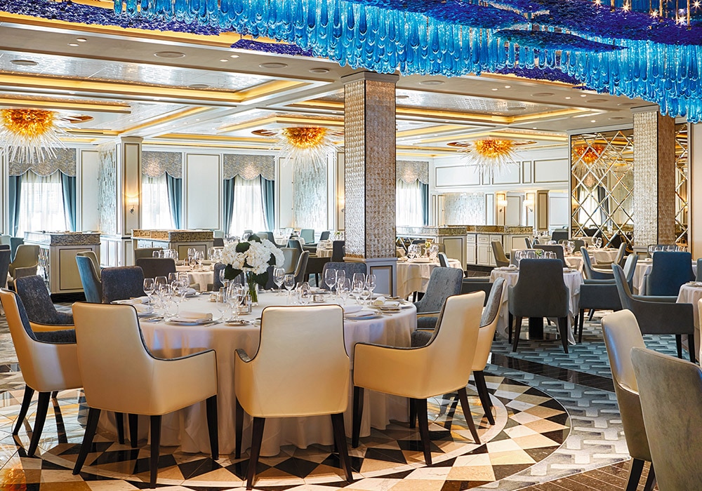 Elegant banquet hall with round tables set for a formal dinner, white tablecloths, floral centerpieces, and blue ceiling decorations.