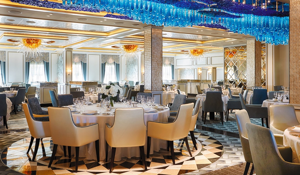 Elegant banquet hall set for a formal dinner with round tables, white tablecloths, floral centerpieces, and blue ceiling decor.