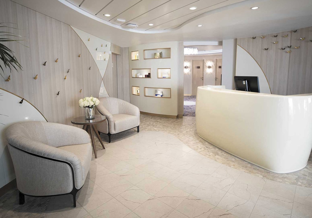 Modern hotel lobby with a curved white reception desk and cream upholstered chairs in a waiting area.