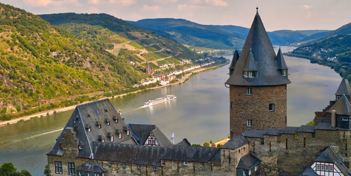 Medieval castle overlooking a winding river and green hills with a boat passing below.