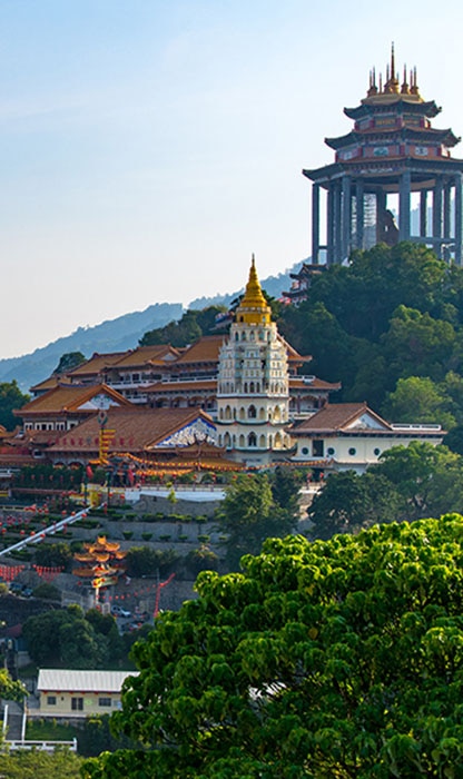 Temple complex on a hillside featuring a white multi-tiered pagoda-like structure and a tall hilltop pavilion surrounded by green trees and orange-roofed buildings.