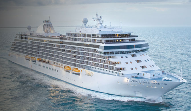 Large white cruise ship cruising on calm blue ocean, viewed from the bow/right side.