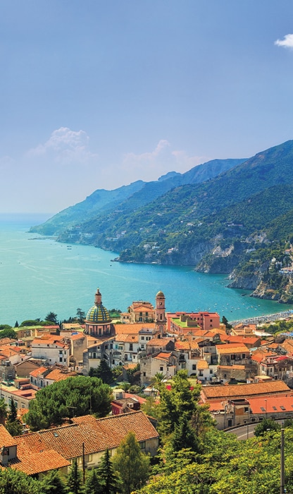 Coastal town with orange-roofed buildings along a turquoise sea and steep cliffs