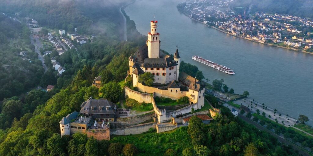 Castle perched on a hill overlooking a winding river with a boat nearby