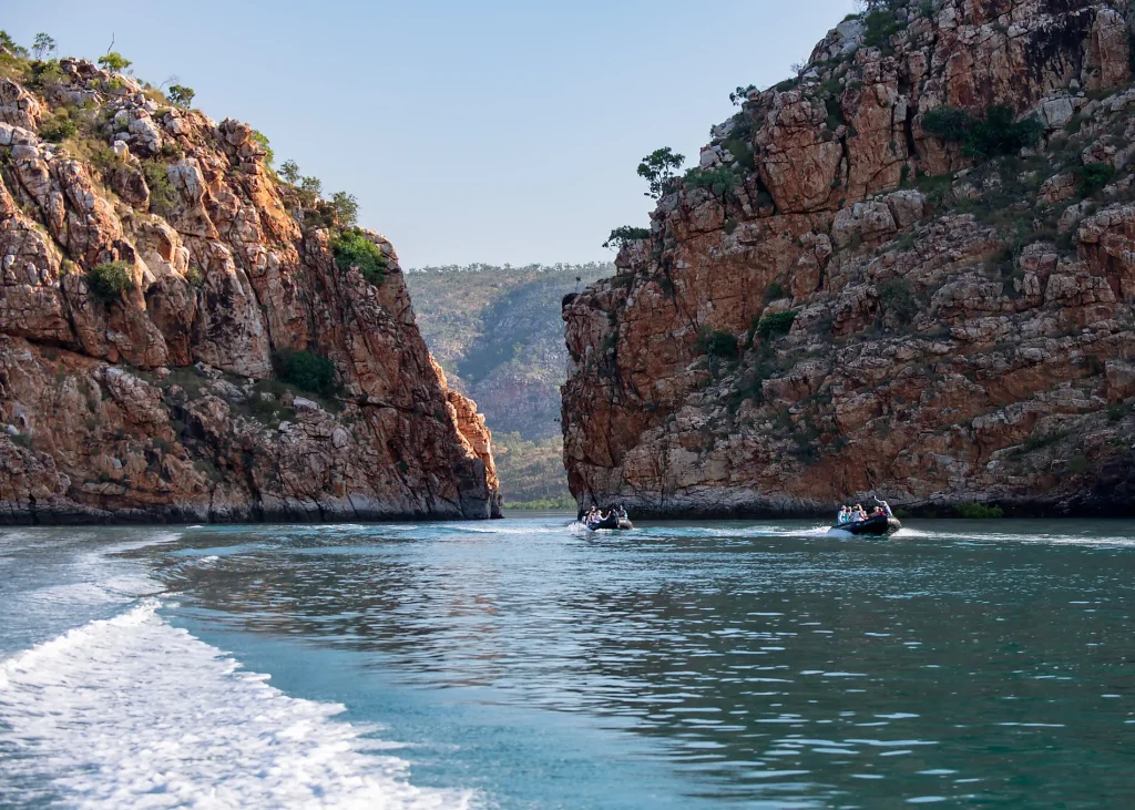 River runs between tall rocky canyon walls with small boats and people on the water.