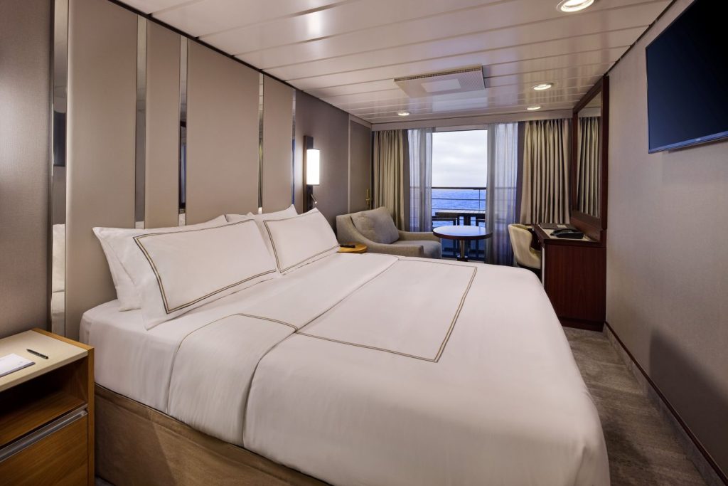 Luxurious hotel room with a king-size bed, seating area, and balcony overlooking the ocean.