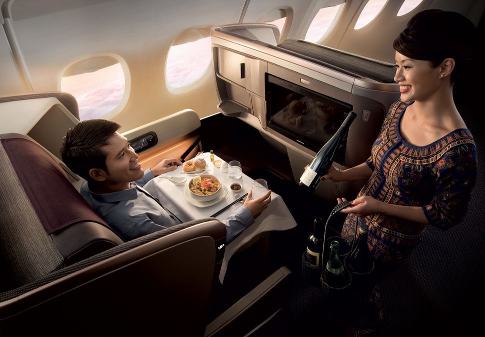 Flight attendant pours champagne for a passenger in a deluxe airplane cabin during a meal service.