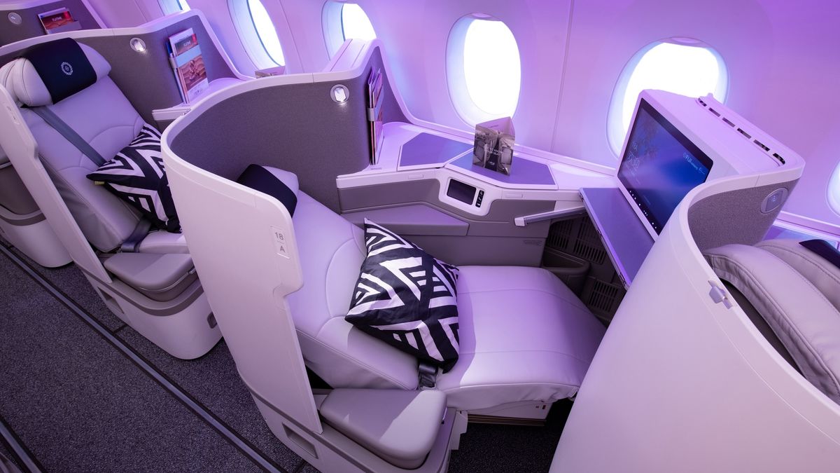 Business class private pod on a modern airplane, with white leather seats, purple ambient lighting, and a large window view panel.